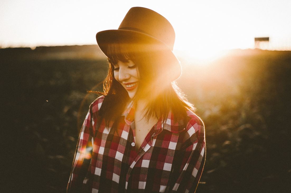 Zdjęcie dziewczyny w kapeluszu w promieniach słońca. Uśmiecha się.